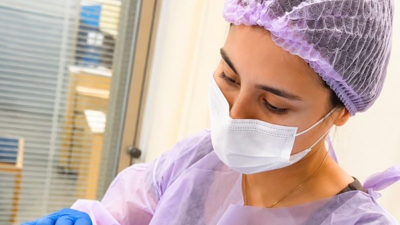 Dra. Roberta Sayuri, médica (CRM-SP 213495), preparando material para procedimento, com paramentação completa