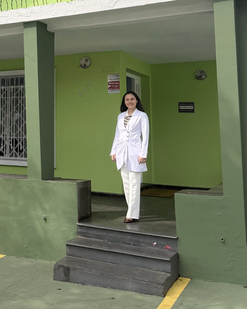 Dra. Roberta Sayuri, de jaleco branco, em pé na entrada do CEMID, na Rua Saturnino Pereira, 317, em Guaianases